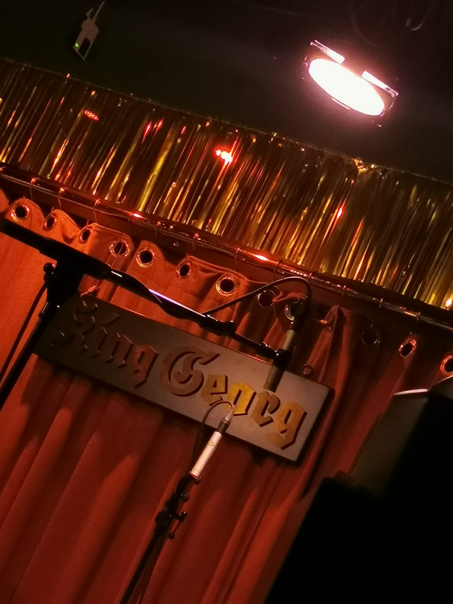 Bild einer Konzertbühne mit einem Mikrophon. Am roten Vorhang hängt das Schild "King Georg".